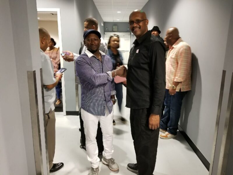 A man shaking hands with another person in a hallway.