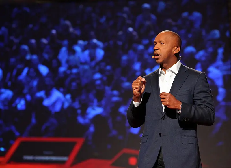 A man in a suit and tie speaking on stage.